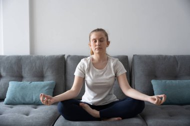 Genç meditasyon yapıyor ve Lotus pozisyonunda kanepede nefes egzersizleri yapıyor.