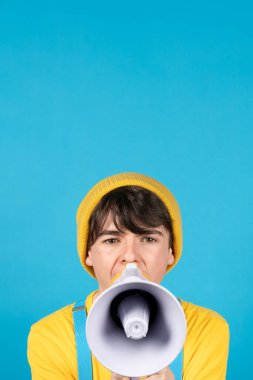 Mavi arka planda megafonla bağıran sevimli genç çocuk.