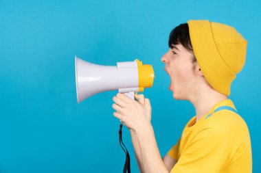 Genç çocuk mavi arka planda megafon ya da hoparlör kullanarak yan tarafa bağırıyor..