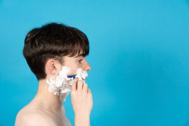 Mavi arka planda sakal tıraşı olan çocuğun yan görünümü