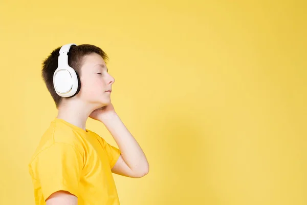 コピースペースで黄色の背景に隔離された目を閉じたヘッドフォンでリラックスした音楽を聞く少年のサイドビュー — ストック写真