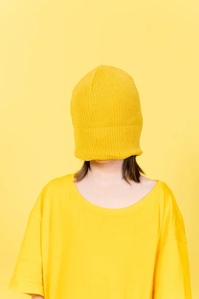 大きなサイズのTシャツと黄色の背景に隔離されたウールの帽子を身に着けている目隠しされた女の子の肖像画 — ストック写真