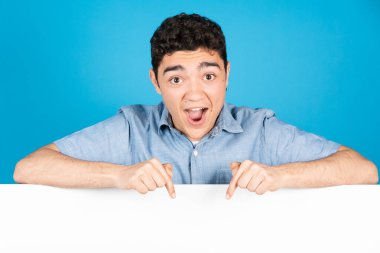 Şaşırmış İspanyol genç çocuk mavi arka planda izole edilmiş fotokopi alanını işaret ediyor..