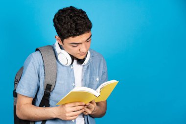 İspanyol üniversite öğrencisi mavi arka planda izole edilmiş bir kitap okuyor..