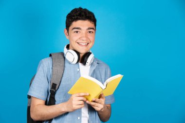 Mavi arka planda izole edilmiş bir kitap tutan İspanyol üniversite öğrencisinin portresi.