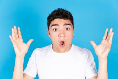 Mavi arka planda, sürpriz yüzlü ve elleri havada İspanyol bir gencin portresi..
