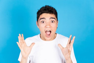 Mavi arka planda izole edilmiş şaşkın İspanyol bir gencin portresi..