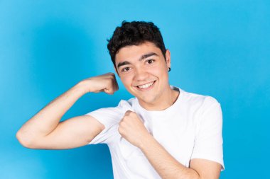 Gülümseyen İspanyol adam mavi arka planda kaslarını gösteriyordu. Ergenlik konseptinde sağlıklı yaşam tarzı