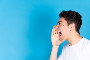 Latin kökenli genç çocuk, mavi arka planda izole edilmiş alanı kopyalamak için el ele bir mesaj veriyor..