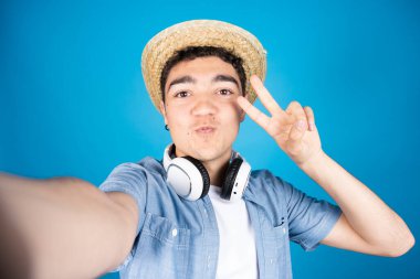 İspanyol genç adam mavi arka planda izole edilmiş bir selfie çekerken barış işareti yapıyor..