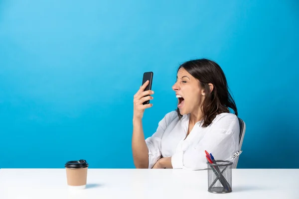 Angry Hispanic Young Woman Shouting Phone Sitting Desk Isolated Blue — Stockfoto