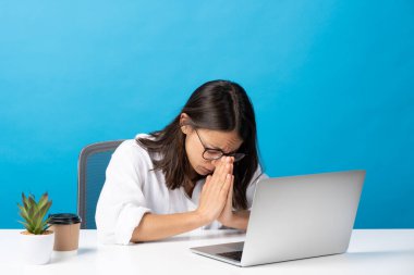 Hispanic pretty young woman praying at laptop isolated on blue background.
