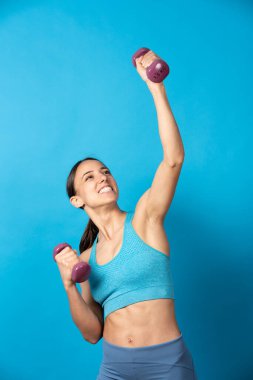 Mavi arka planda izole edilmiş yükselen mutlu sporcu kadın. Formda bir kadın egzersiz yapıyor..