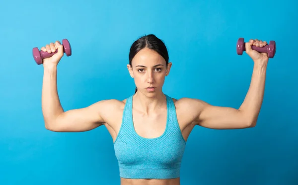 Fit Hispanic Sportswoman Rising Weights Looking Camera Isolated Blue Background — Fotografia de Stock