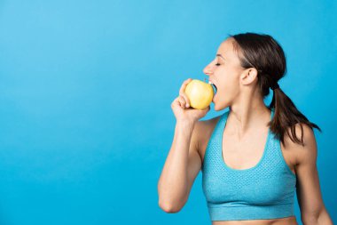 İspanyol sporcu kadın, mavi arka planda izole edilmiş fotokopi alanı olan elmayı ısırıyor..