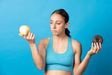 İğrençsin İspanyol sporcu kadın. Meyveye bakıyor ve elinde çikolatalı çörek tutuyor..