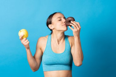 İspanyol sporcu kadın çikolatalı donut sürüyor ve mavi arka planda elma tutuyor..