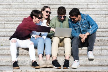 High school students having fun using laptop. Students sitting on stairs