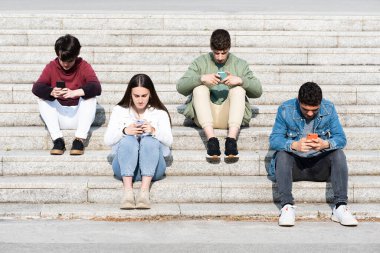 Teenager friends sitting on stairs and using their phones. Digital addiction and social distancing concept.