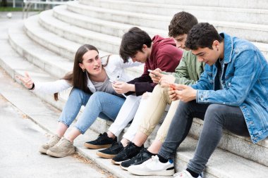 Teenager girl asking for attention to group of friends concentrated on phones. Digital addiction and social distancing concept.