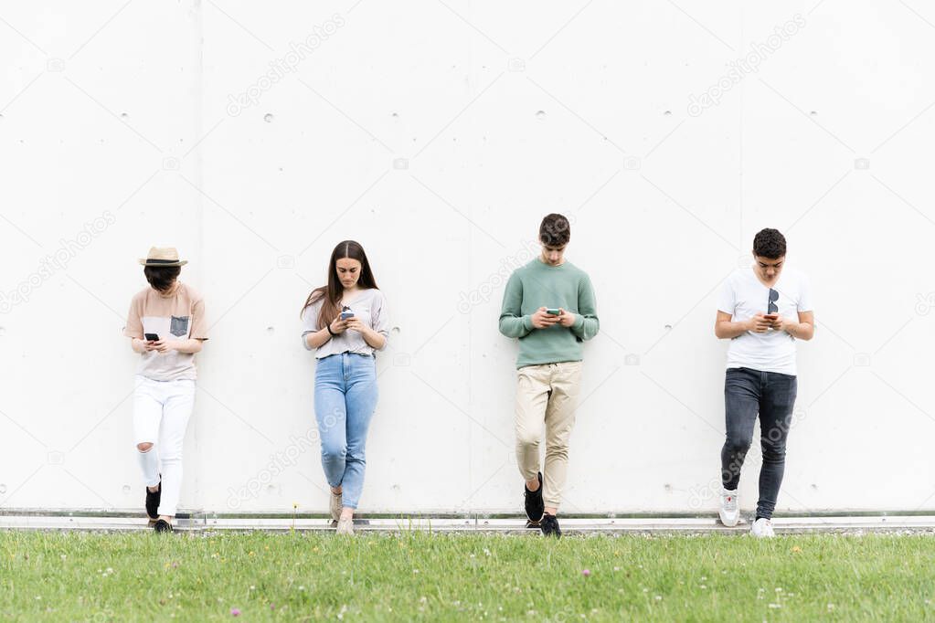 Teenagers against a wall using their phones. Students concentrated on social media. Digital addiction and social distancing concept.