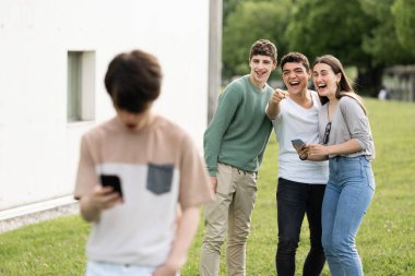 Bir grup genç gülüp oğlanı işaret ediyor. Siber zorbalık kavramı