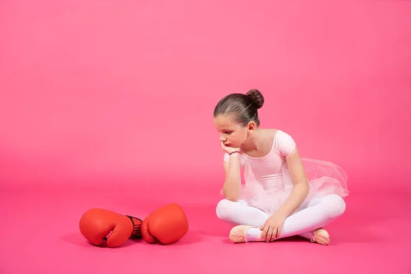 バレエダンサーの子供ボクシングの手袋を見て 若いです女の子座っています上の階でAスタジオショットで鮮やかなピンクの背景 — ストック写真