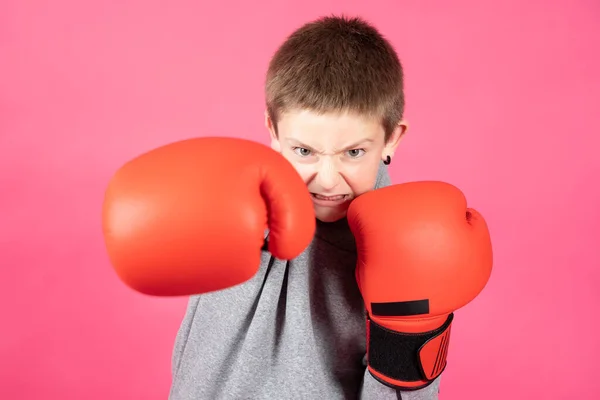 Angry boy wearing boxing gloves punching and looking at camera isolated on vivid pink background