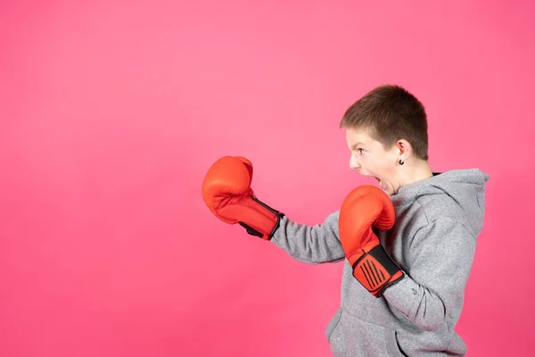 Side view of aggressive teenager boy wearing boxing gloves isolated on colorful pink background. Violence on childhood concept