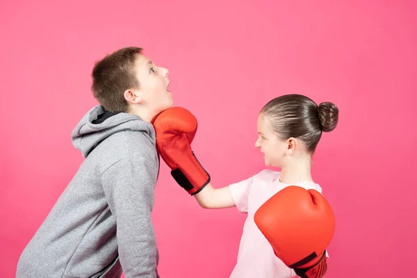 Bullied little girl taking revenge of older boy. Child wearing boxing gloves hitting bully isolated on pink background. Woman power and self defence concept