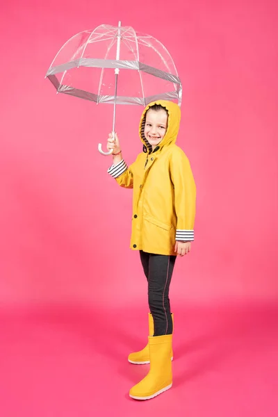 黄色のレインコートを着た少女の全身肖像画とピンクの背景に隔離された傘を持っています 悪天候の概念 — ストック写真