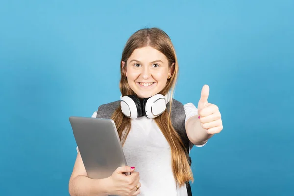 Pretty college student making ok sign and holding laptop isolated on blue background. Back to school concept.