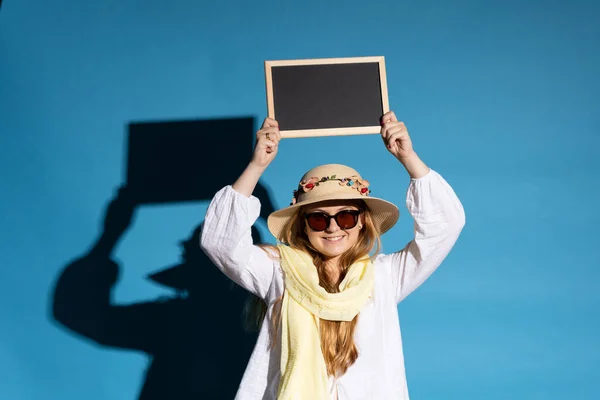 青い背景に隔離された晴れた日に上記の黒板を保持観光女性 — ストック写真