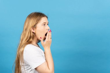 Mavi arkaplanda izole edilmiş kopyalama alanına bakan şaşırmış sarışın kadının yan görüntüsü.