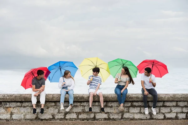 Group Friends Talking Sitting Wall Holding Colorful Umbrellas — Stockfoto