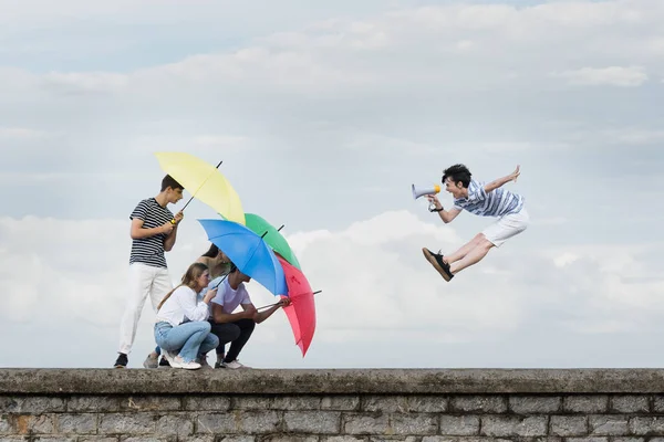 毒性のあるコメントを無視する抽象概念 Teenager Boy Shouting Megaphone Friends Protecting Themselves Using Umbrellas — ストック写真