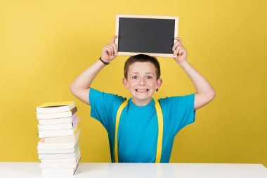 Öğrenci çocuk, sarı arka planda, kafasının üstünde kopya alanı olan karatahta kaldırıyor..