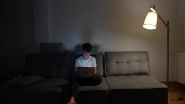 Genç bir çocuk gece oturma odasında çalışıyor. Genç öğrenci dizüstü bilgisayarın önünde esniyor ve esniyor. Aşırı çalışma kavramı.