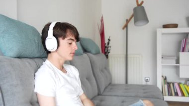 Teenager boy listening relaxing music on headphones while sitting on couch at home