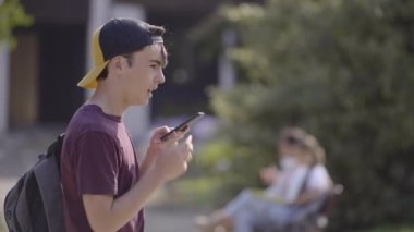 Teenager student boy sending voicemail outdoors in a park.
