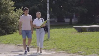 Teenager friends walking outdoors in a park, then boy jumping at back. Having fun and carrying piggyback. Friendship concept.