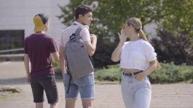Homophobic teenager girl insulting and making fun of gay couple. Students walking holding hands in a park.