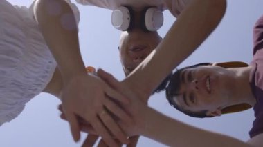 Low angle view of teenagers handshaking and raising hands. Cooperation, teamwork and team spirit concept