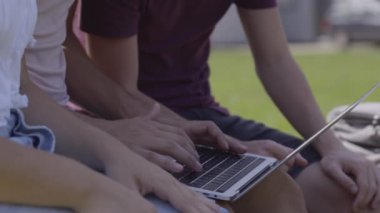 Closeup of friends using laptop and typing outdoors in a park. Students working together.