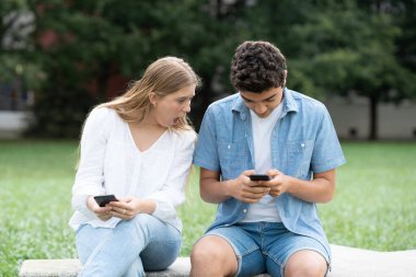 Şaşırmış genç bir kız parkta cep telefonundan erkek arkadaşına gözetliyor. Sosyal medya gizlilik kavramı.