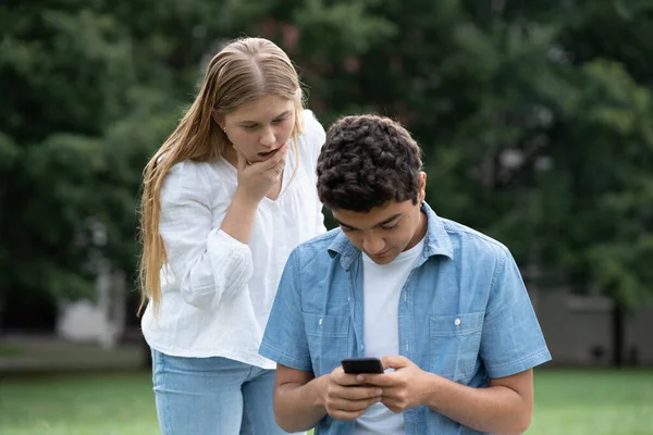 十代の女の子立って後ろ男の子とスパイ携帯電話屋外でA公園 — ストック写真