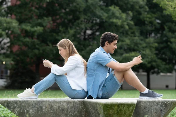 10代のカップルが後ろに座って 公園で屋外で電話を使用しています デジタルとソーシャルメディア中毒の概念 — ストック写真