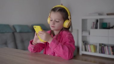 Evde telefon kullanarak kulaklık takan sevimli küçük kız.