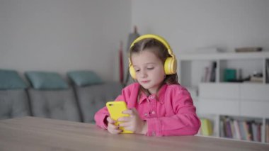 Kulaklık takan, telefon kullanan ve evde selfie çeken sevimli küçük bir kız..