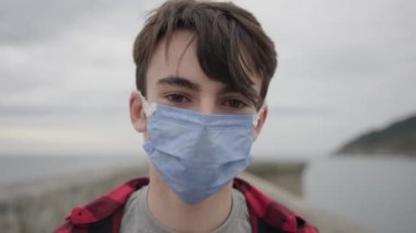 Genç çocuk, Coronavirus salgını sırasında cerrahi maskesini çıkarıyor ve kameraya bakarken nefes alıyor..